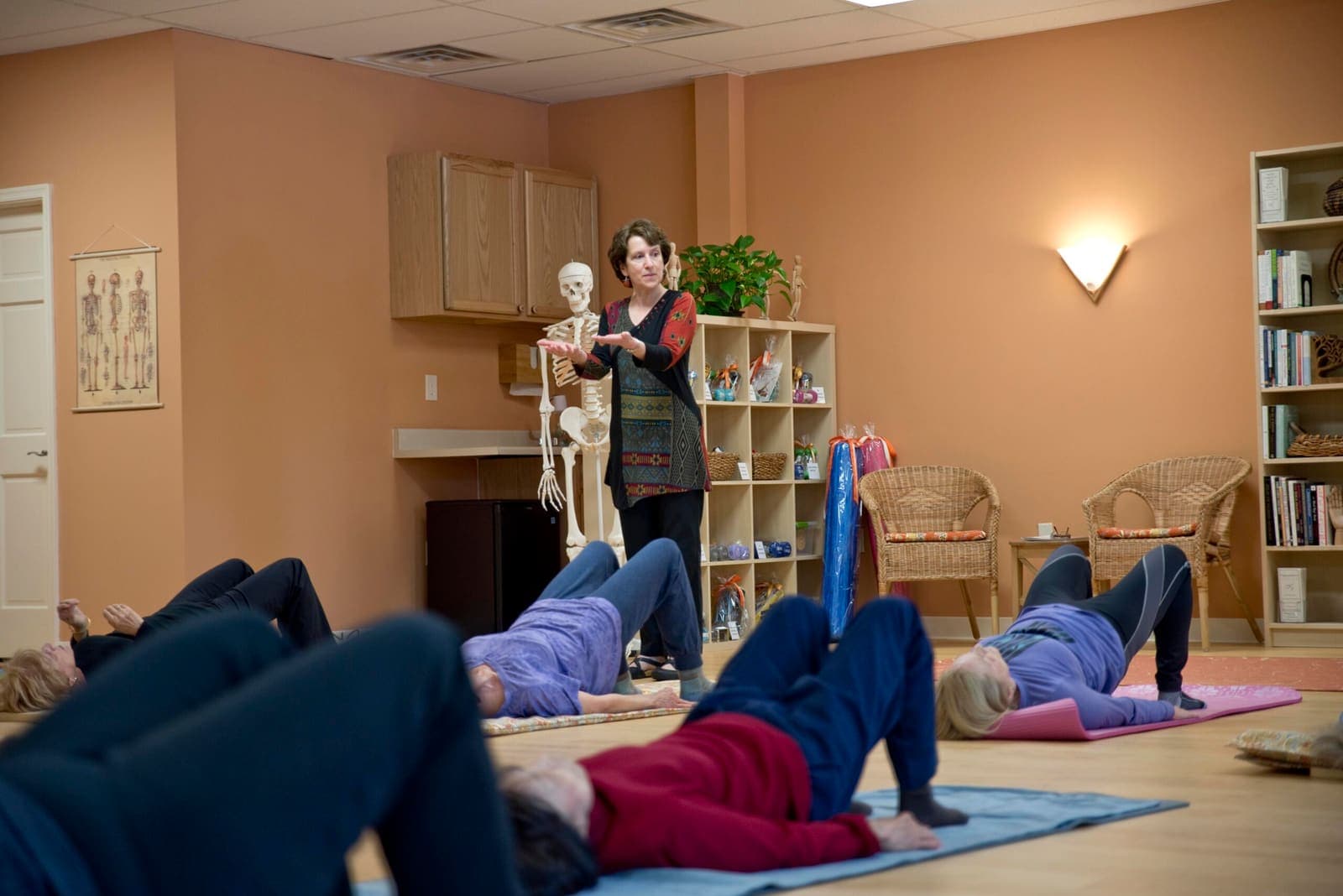 Students on mats lifting their hips while Joanne teaches beside an anatomical skeleton