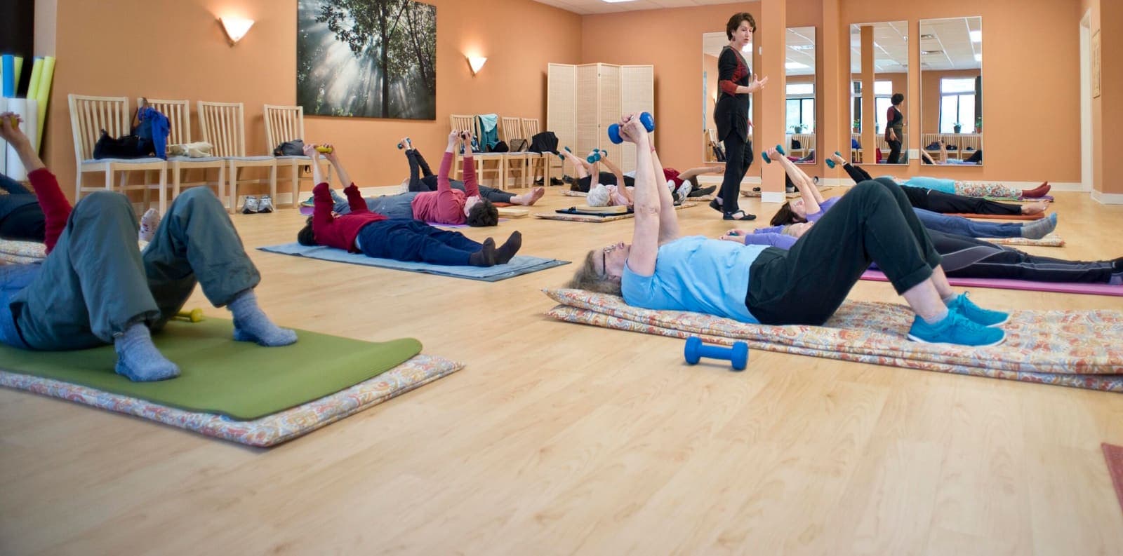 A row of students lying on mats with foam rollers, working through a floor sequence