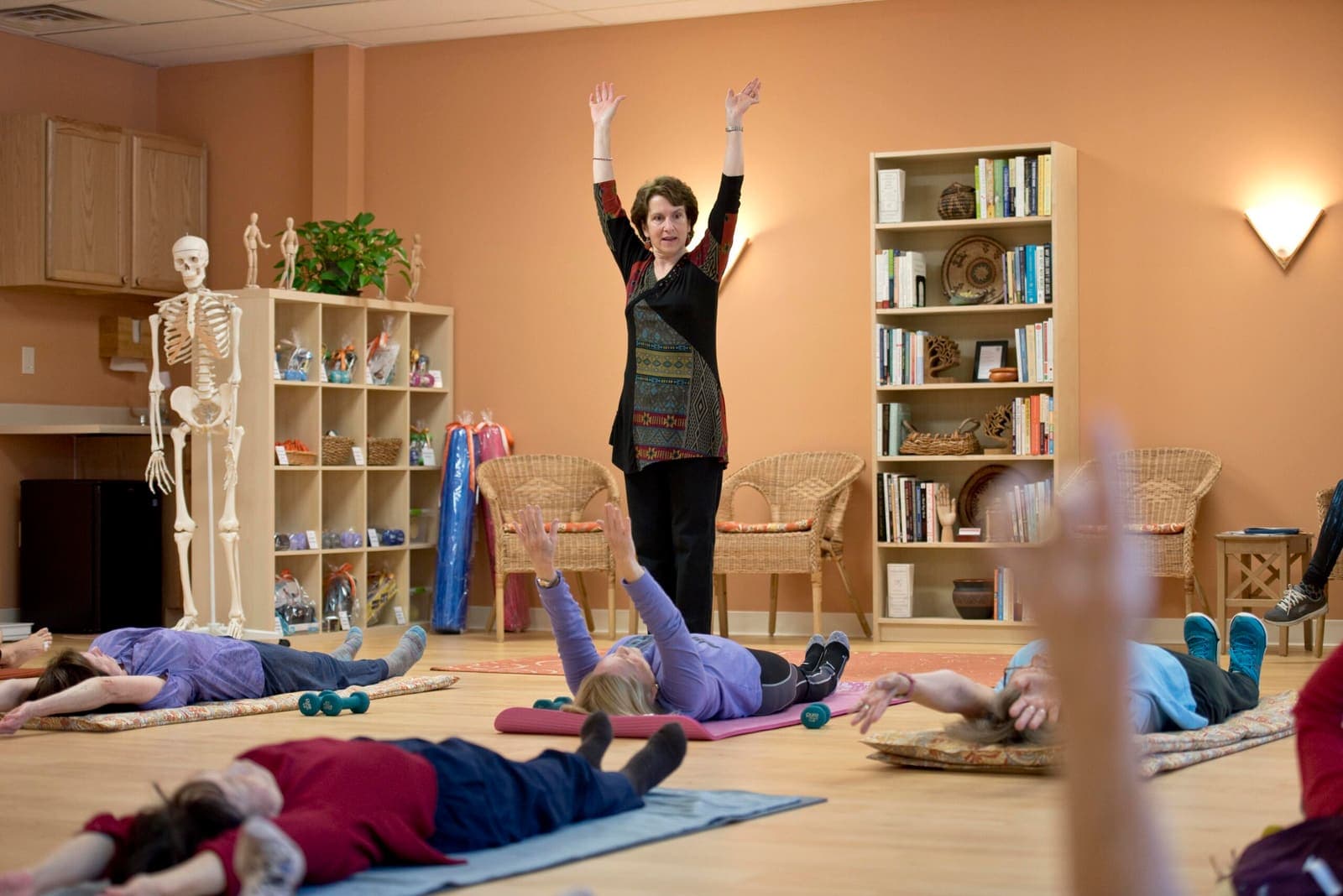 Joanne demonstrating an overhead reach while the class follows along on mats
